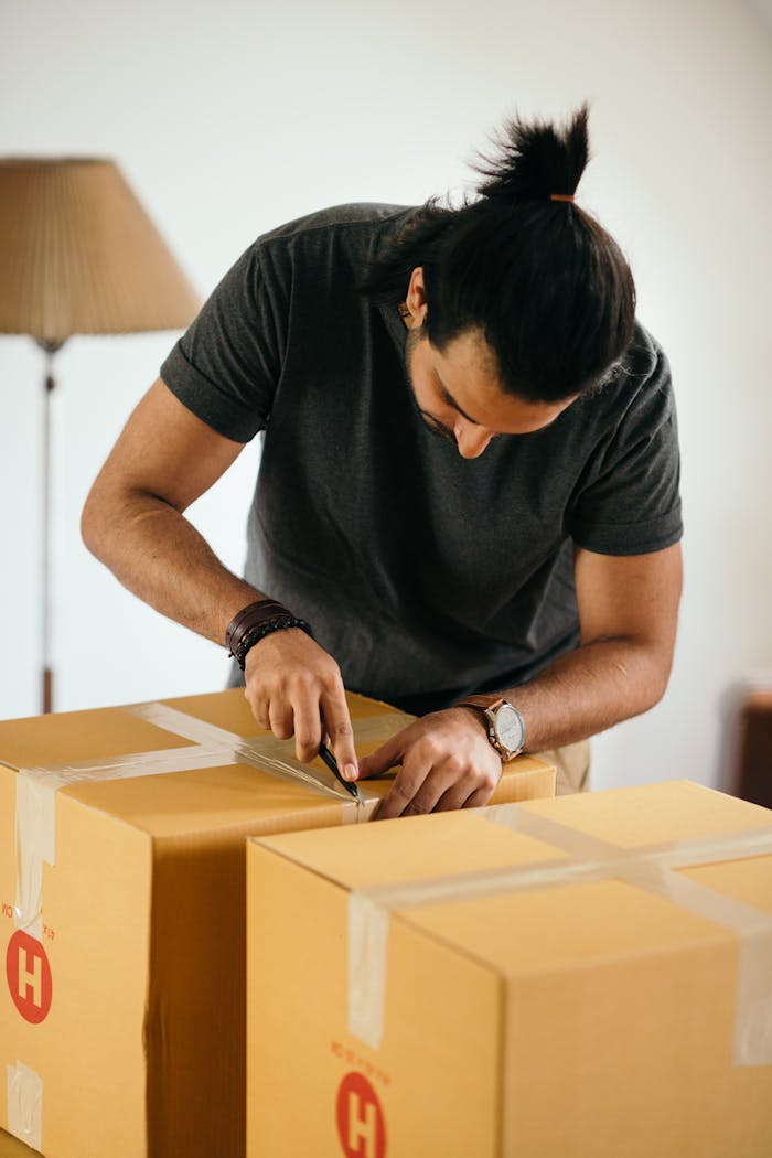 Serious male using cutter while carefully unpacking carton box with belongings moving house